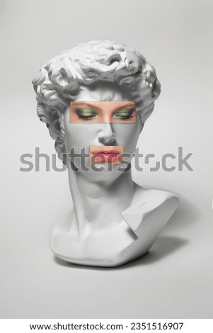 Replica of the head of an antique statue of David with a taped eyes and mouth with makeup on white background. Woman lips and eyes with makeup on statue. Royalty-Free Stock Photo #2351516907