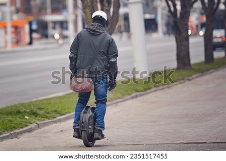 Man in protective gear riding electric unicycle, monocycle or mono wheel. Man in helmet on electric vehicle, view from back. Riding electric mono wheel, personal electric transport Royalty-Free Stock Photo #2351517455