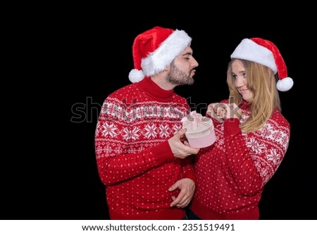 Boy cade pose of kissing a girl with a gift in her hand the girl has a disapproved face. Couple dressed in sweater and christmas hat. concept couple quarrel at christmas new year, bad gift.
