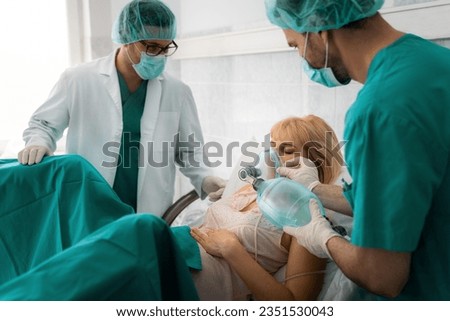 Young mother getting ready to give birth to her child while two assistants are helping her. Male doctor and technician wearing scrubs and lab coat assisting pregnant woman to breathe.