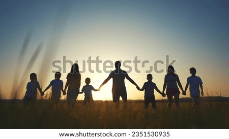 large family walks across field holding hands. happy family childhood dream concept. family walks across the field on the grass lifestyle at sunset and hold each other's hands dark silhouettes Royalty-Free Stock Photo #2351530935