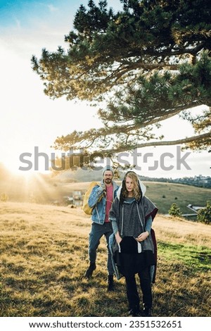 Vertical photo of a couple of hikers walking along mountain grassy trail and spending their time together in the nature. Portrait of man and woman walking through pathway on mountain. Copy space.