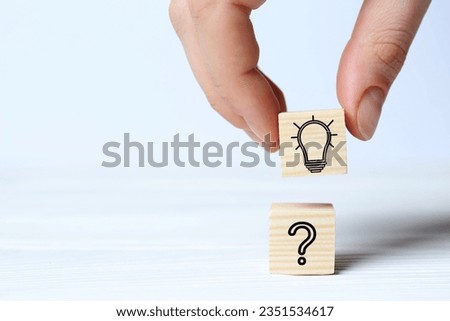 Idea concept. Woman putting cube with illustration of light bulb to another one with question mark on white wooden table, closeup
