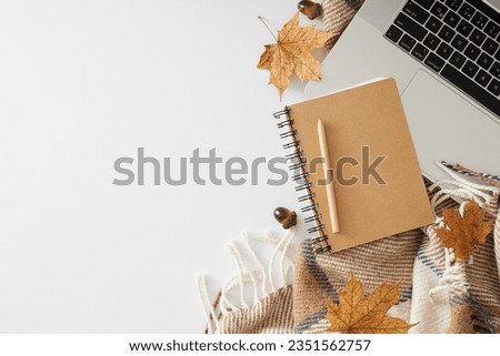 Embracing the snugness of fall in a home office. Top view photo of cozy blanket, pen, copybook, laptop, acorns, dry autumn leaves on white background with empty space for ad or note