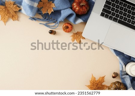 Autumn-enriched workspace. Top view photo of patchy blanket, laptop, candle, pumpkins, acorns, dry autumn leaves on pastel beige background with empty area for promotion or wording