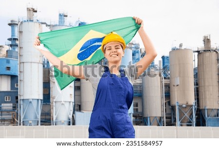 Cheerful female worker in hardhat with brazilian flag standing in front of factory Royalty-Free Stock Photo #2351584957