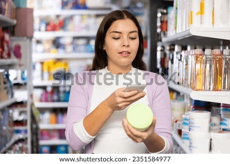 Woman photographing skin or hair care product with smartphone while standing in beauty store