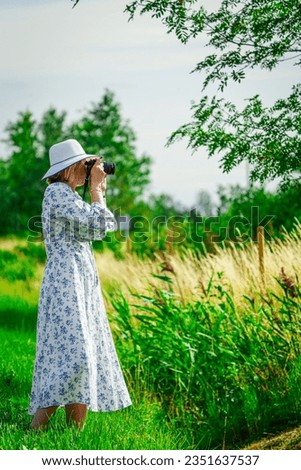 Side view of calm young female traveler in casual summer clothes taking photo of nature. Woman is a professional photographer with dslr camera, outdoor.