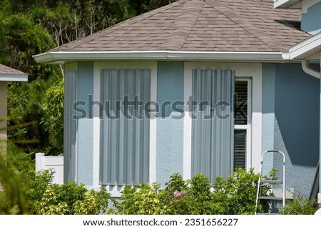 Boarded up windows with steel storm shutters for hurricane protection of residential house. Protective measures before natural disaster in Florida Royalty-Free Stock Photo #2351656227