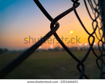 Defocus blur  Silhouette of chain link Fence grills rust texture background for text  with sunset bokeh  behind the barbed wire fence strange blue glow in evening sky after sunset.