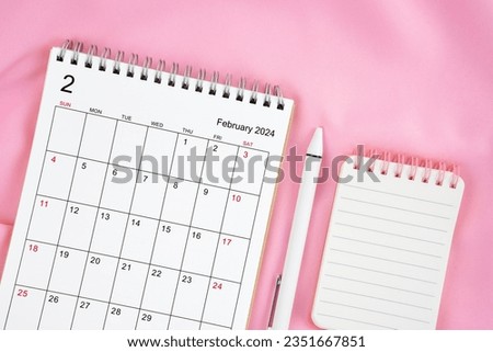 February 2024 month calendar and pen with open diary on pink fabric background. Monthly calendar concept.