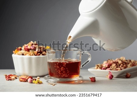 Herbal tea is poured into a mug. Mixtures of dried herbs and flowers are scattered on the stone table. Royalty-Free Stock Photo #2351679417