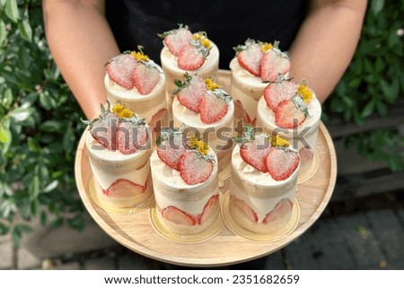 Woman holding plate with delicious Strawberry shortcake. 
Shortcake on a wooden plate. Fresh Strawberry topping with cream and yellow flower. Bakery picture free space for text.