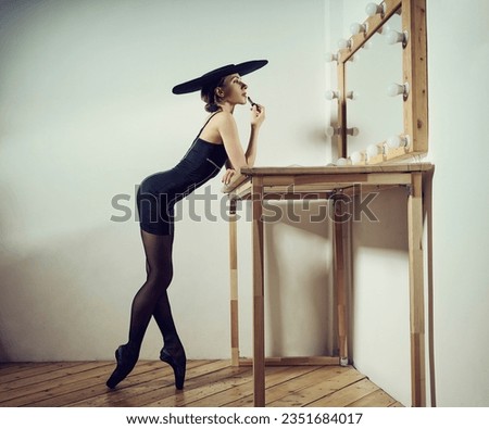 a ballerina in the style of fashion total black in a dress and hat paints her lips with red lipstick at the mirror