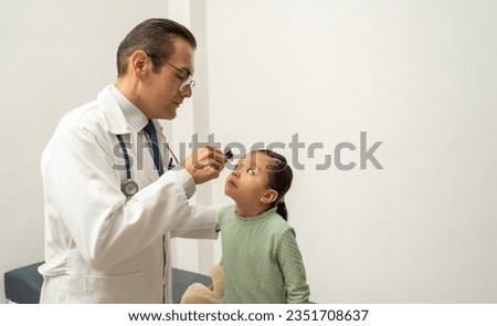 hispanic doctor checking on girl pupil with light lantern