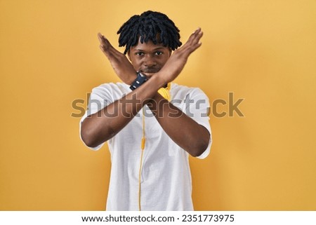 Young african man with dreadlocks standing over yellow background rejection expression crossing arms doing negative sign, angry face 