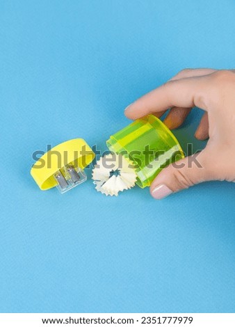 Close-up of a young woman sharpening a training slate pencil in a  yellow plastic sharpener on a blue background