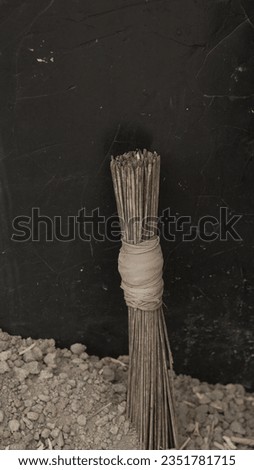 Artistic Arrangement of Stacked Palm Broomsticks on Black Background, Discover the captivating composition of neatly piled palm broomsticks casting intricate shadows against a sleek black backdrop.