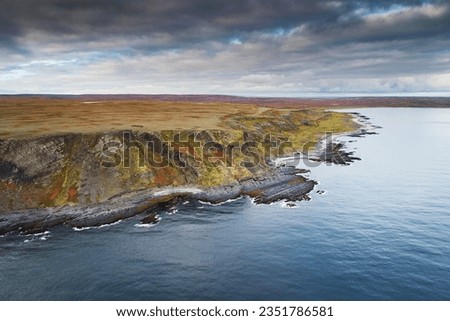 Top view of the rocky coast of the Barents Sea against a blue sky on a bright cloudy day. Aerial photo of landscape