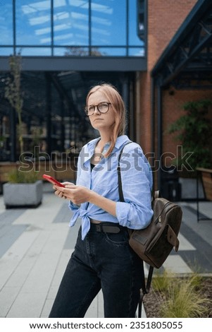 Thoughtful Caucasian woman keeps hand on chin looks pensive above poses against business build background blank copy space for your advertising content thinks about future. High quality photo