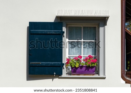 Idyllic view of window with wooden shutter and plant pot decoration with red flowers on a hot summer day at Swiss City of Zürich. Photo taken August 24th, 2023, Zurich, Switzerland.