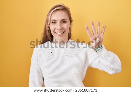 Young caucasian woman wearing white sweater over yellow background showing and pointing up with fingers number four while smiling confident and happy. 