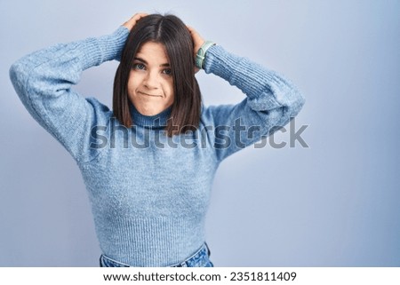 Young hispanic woman standing over blue background doing bunny ears gesture with hands palms looking cynical and skeptical. easter rabbit concept. 