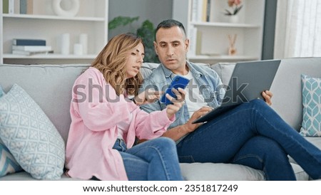 Man and woman couple using laptop and smartphone sitting on sofa at home Royalty-Free Stock Photo #2351817249