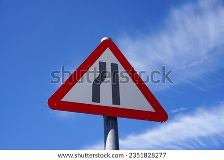 Road narrowing left sign in city. Triangular warning sign for motorists informing road narrows ahead on the left