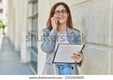 Young woman business worker talking on smartphone reading document at street