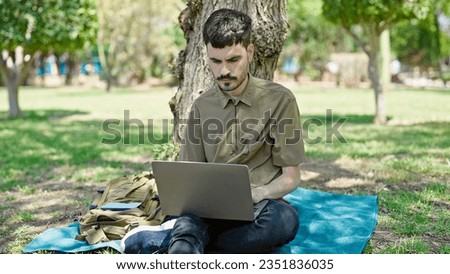 Young hispanic man using laptop sitting on floor at park