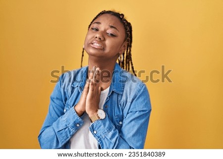 African american woman with braids standing over yellow background begging and praying with hands together with hope expression on face very emotional and worried. begging. 