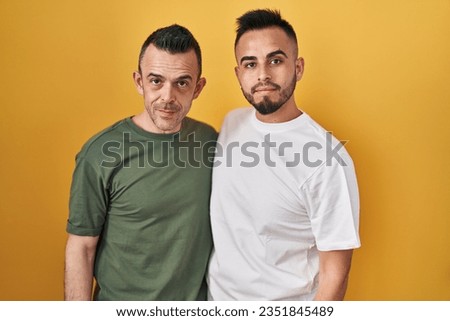 Homosexual couple standing over yellow background relaxed with serious expression on face. simple and natural looking at the camera. 