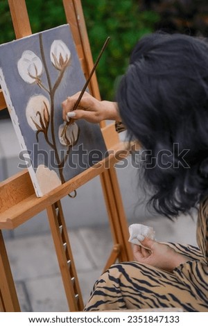 A young girl artist paints picture with a brush on a canvas that stands on an easel view from behind the back