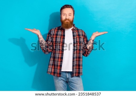Portrait of cheerful optimistic man with tattoo wear plaid shirt palms demonstrate products empty space isolated on blue color background