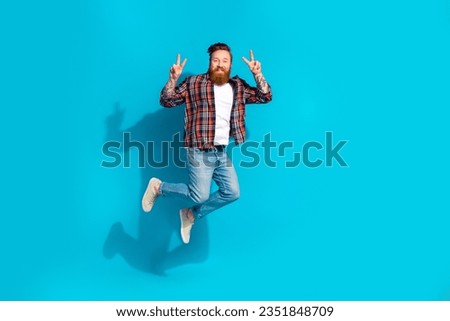 Full length photo of good mood handsome man dressed plaid shirt denim pants showing v-sign flying isolated on blue color background