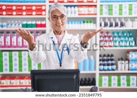 Middle age woman with tattoos working at pharmacy drugstore smiling cheerful offering hands giving assistance and acceptance. 