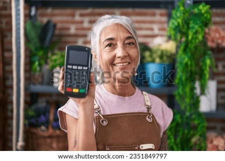 Middle age woman with tattoos working at florist shop holding dataphone looking positive and happy standing and smiling with a confident smile showing teeth 
