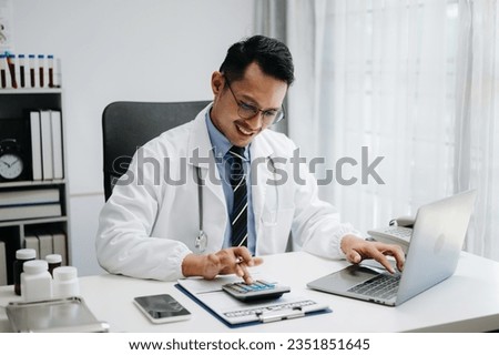 Healthcare costs and fees concept. Asoian Hand of smart doctor used a calculator and smartphone, tablet for medical costs at hospital in morning light

