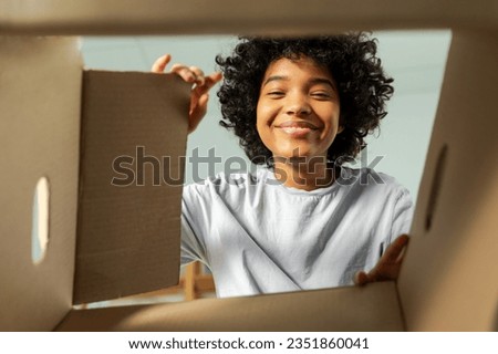 Inside of cardbox bottom view. African girl unpacking delivery looking in box. Woman opening carton box. Female getting parcel looking at delivered goods items. Satisfied client positive feedback Royalty-Free Stock Photo #2351860041