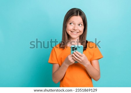 Photo of cheerful small girl wear stylish orange t-shirt hold smartphone look at sale empty space isolated on teal color background