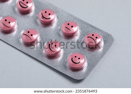 Pink pills with different emotional faces in blister on light grey background