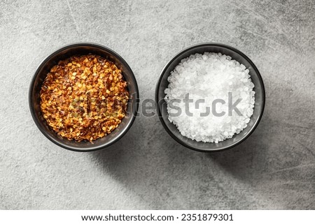 Dry chili pepper flakes and salt. Crushed red peppers in bowl on the black table. Top view.
