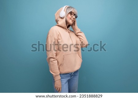 stylish 60s granny with gray hair masters technique and listens to music in headphones on a studio background with copy space