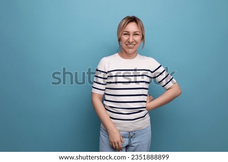 optimistic photo of a positive cheerful blond girl in a striped sweater on a blue background with copy space