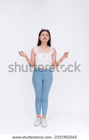 A young asian woman trying to keep calm and avoid stress by meditating and closing her eyes. A novice yoga practitioner. Full body photo isolated on a white background.