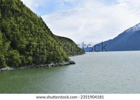 beautiful flush green grassy forest mountain across the alaskan ocean from a snowy ice encrusted mountain glacier in skagway from an alaskan cruise