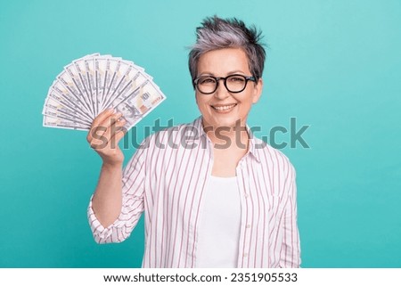 Photo of optimistic middle age businesswoman holding jackpot dollars usd banknotes millionaire isolated on aquamarine color background