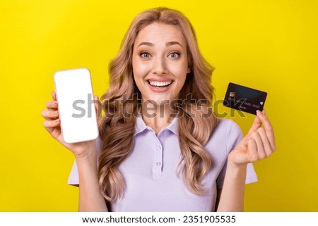 Photo of attractive astonished lady toothy smile hold show debit card empty space smart phone display isolated on yellow color background