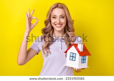 Photo of toothy beaming girl with curly hairstyle wear violet polo hold house show okey approve isolated on yellow color background